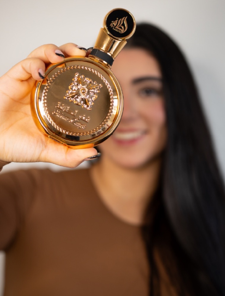 Mujer sosteniendo un perfume dorado frente a la cámara