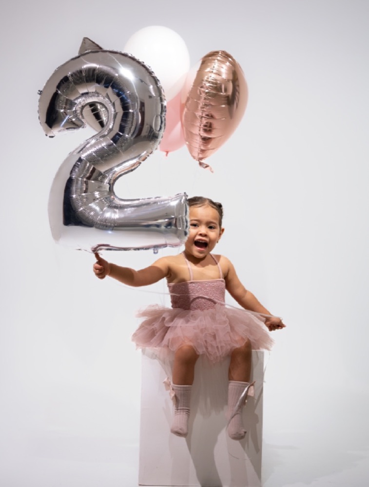 Niña celebrando su segundo cumpleaños con globos plateados